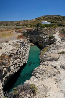 Rocky landscape with clear water and small white house under blue sky, volcanic island, island,