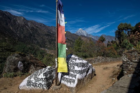Buddhist prayer flag and holy mantras on manistones in front of mountain landscape on the way to