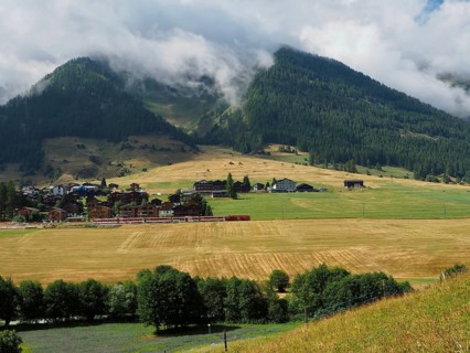 Village surrounded by fields and forest, surrounded by steep mountain slopes and cloudy peaks,