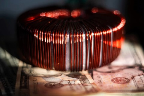 Industrial copper wire coil placed near US dollar bills, symbolizing the link between technology,