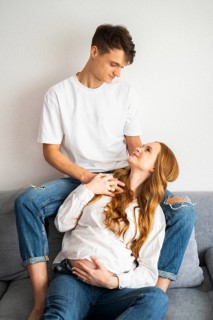 A young couple expecting a baby share a loving and tender moment on the sofa. The woman embraces