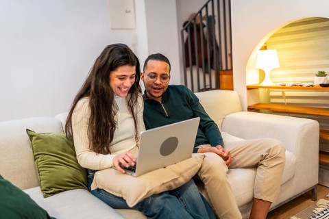 Smiling diverse couple connecting and enjoying digital content on a laptop while relaxing