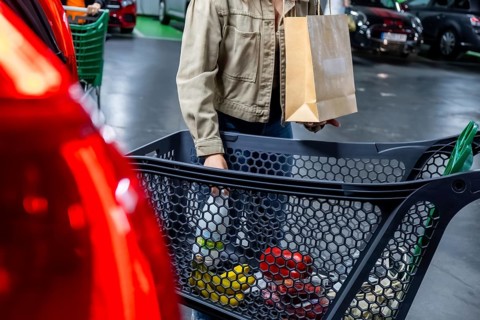 Customer shopping at a supermarket, carrying a paper shopping bag and pushing a cart full of