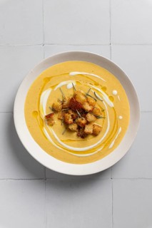 A close-up of creamy cauliflower curry soup garnished with crispy croutons and rosemary Presented
