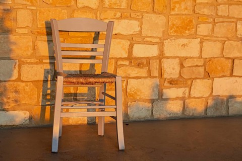 Greek kafenio chair in front of a sunlit sandstone wall, Cyprus