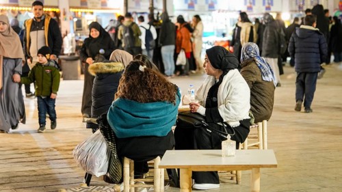 Muslim families and individuals gather at outdoor tables for a mass community Iftar meal under
