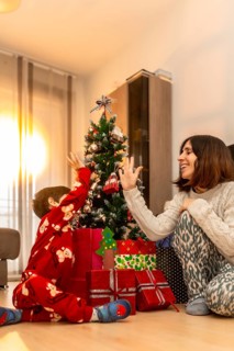 Happy mother and son bonding, wearing pajamas, and giving a high five next to a decorated christmas