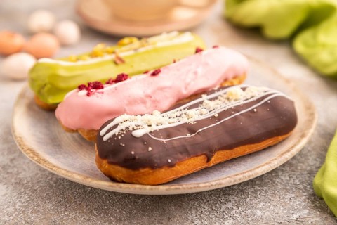 Glazed Eclairs on brown concrete background and green linen textile, cup of coffee, side view,
