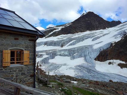 Stone house, mountain hut next to impressive glacier and snow-capped mountains, E5, hiking in the