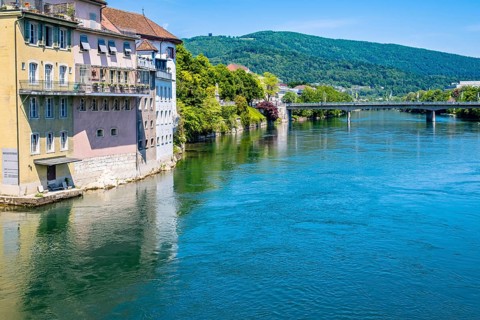 Riverfront cityscape with historic architecture and a bridge surrounded by green countryside and