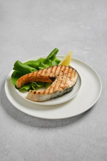 Salmon fillet on white plate with fresh salad leaves and slice of lemon. This dish is ready to be