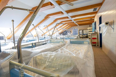 Several hospital beds under wooden ceiling in a storage room with natural light, old disused
