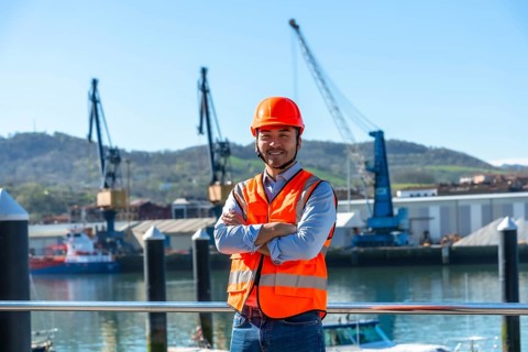 Asian male port worker standing confidently with arms crossed in orange hard hat and safety vest at