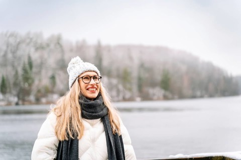Cheerful woman enjoying the winter scenery near a snow-covered lake. A woman wearing a white winter