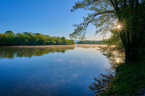 A quiet river with trees on the banks and the sun shining through the leaves. Reflections in the