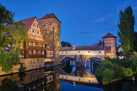 Beautiful twilight view of the illuminated Henkersteg bridge and half-timbered houses reflecting in