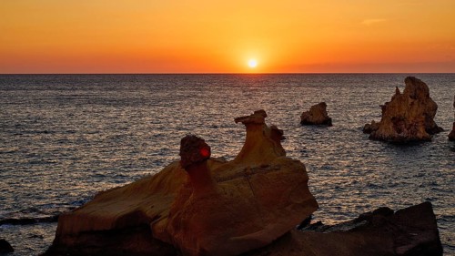 Sunset casts an orange glow over sea and rocks, Aspragremna, White Cliffs, Mavorspilia Beach,
