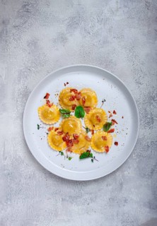 Fresh ravioli, with butter, spices and herbs, fried bacon, on the table, top view, light