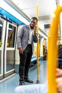 Young businessman engaging in a phone conversation while commuting on a subway train, confidently