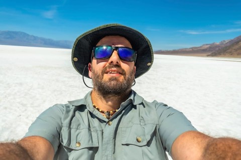 Man wearing a hat and sunglasses taking a selfie at badwater basin in death valley national park,