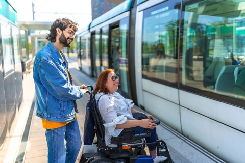 Young man assisting disabled woman in a wheelchair as they board a modern tram in the vibrant city,