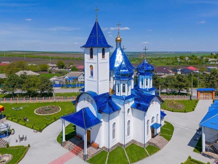 Church with blue roofs and white façade, nestled in a rural setting under a blue sky, aerial view,