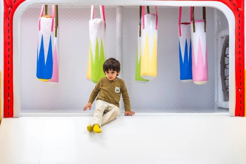 Young child sitting near colorful hanging punching bags in a safe, padded indoor play area designed