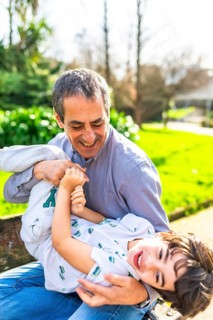 Grandfather and his grandson are having fun in a park, the grandfather is holding the little boy