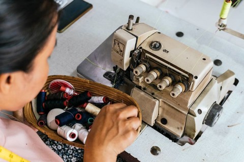 A asian seamstress selects colorful threads from a basket beside an industrial sewing machine,