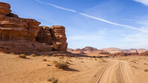 The Wadi Rum desert in Jordan, showcasing sandy terrain, rocky formations, and a clear blue sky. A