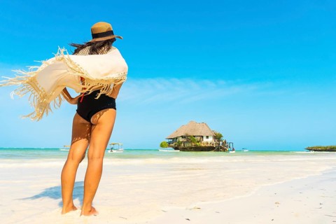 Woman tourist wear bohemian tunic walks across white sandbar toward the iconic Rock Restaurant in