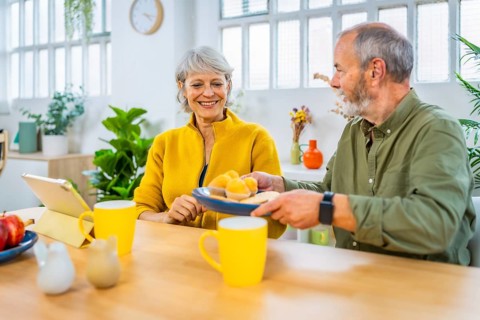 Senior man sharing pastries with his wife at home in the morning