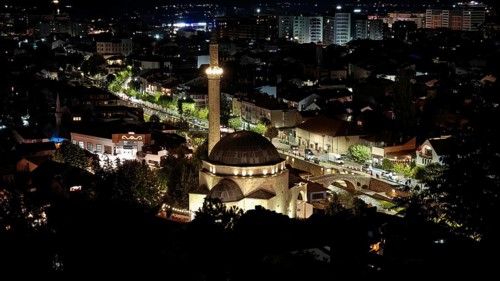 Nighttime cityscape with illuminated mosque and surrounding buildings illuminating the night sky,