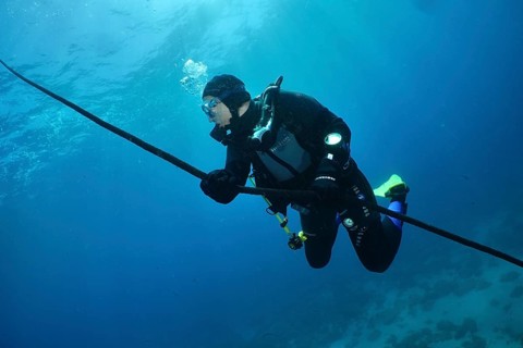 Diver holding on to a rope, floating in the blue underwater. Slow descent along the anchor line.