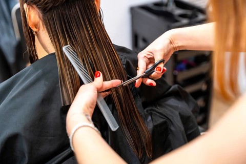 Stylist trims long wet brown hair with scissors and comb in a modern salon, delivering a precise