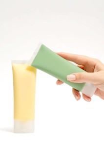 Cropped unrecognizable hands holding green and yellow face mask tubes, rich in natural ingredients.