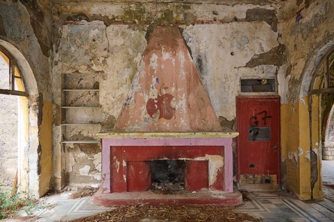 An abandoned fireplace in a dilapidated room surrounded by graffiti and dirty walls, Italian