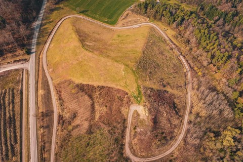 Aerial view of a hilly landscape with a curved path surrounded by trees and fields, old deposit in