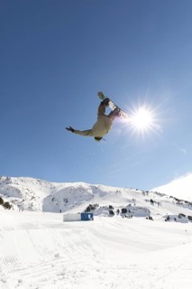A snowboarder performs a daring aerial trick against a stunning mountain backdrop under a clear