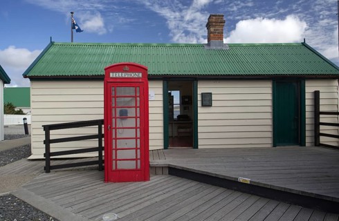 Small hut with a green roof and a classic red telephone box in front of it under a blue sky,
