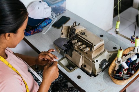 A asian seamstress operates a sewing machine in a textile workshop, focusing on detail. Nearby are