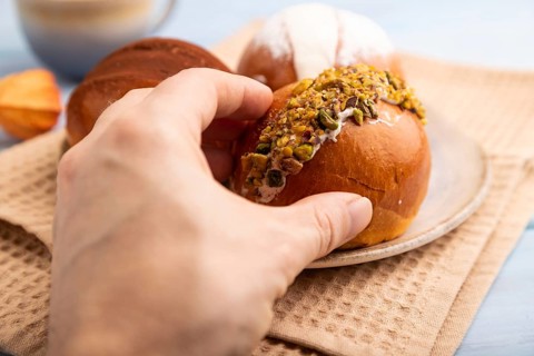 Maritozzo traditional Italian bun dessert with hand, cup of coffee, on blue wooden background with
