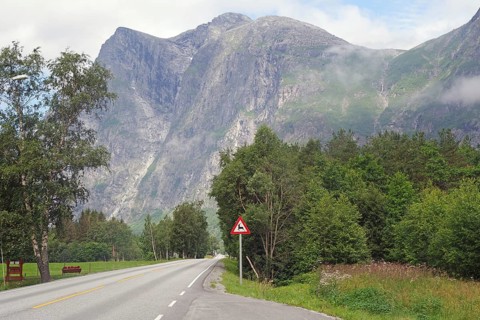 Empty country road surrounded by high mountains and green trees under cloudy sky, Raumadalen,