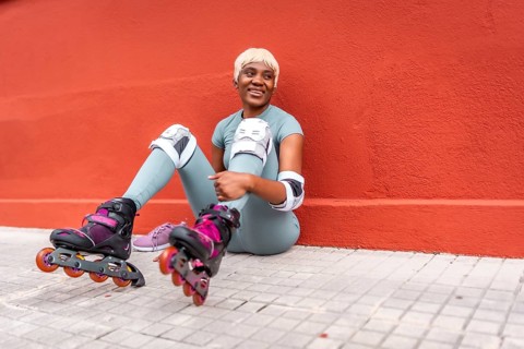 Tired african urban sportive woman sitting on the street wearing inline skates