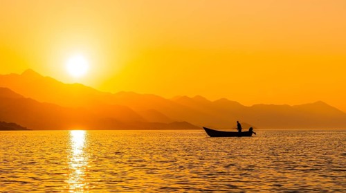 Silhouette of a fishing boat with a fisherman fishing in the orange sunset of Shkoder lake in