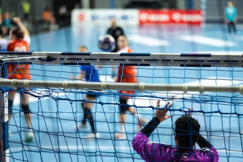 Detail of handball goal crossbar with net and women handball match in the background in Lubin,