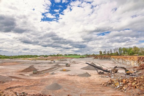Large open-pit quarry with gravel piles, exposed rock walls, and active heavy machinery, Sweden