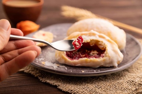 Glazed Pies with Cowberry jam on brown wooden background and linen textile with hand, cup of
