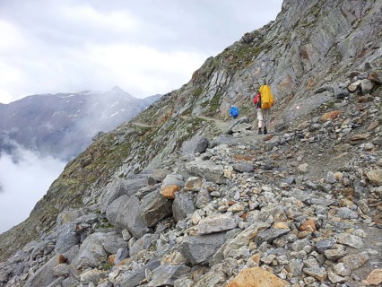 Two hikers with large backpacks climb a rocky mountain trail surrounded by fog, E5, hiking in the