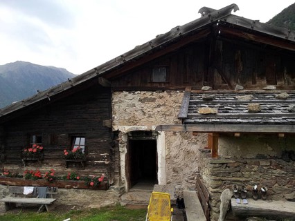 Rustic mountain hut made of stone and wood with flowers on the windows in the middle of the